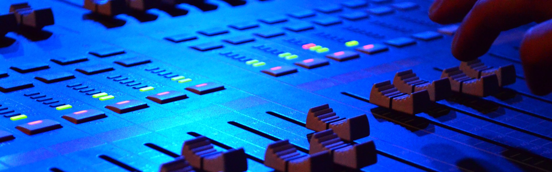 Close view of mixing console faders set at varied levels, with a hand making an adjustment.