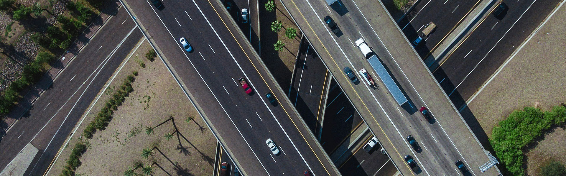 Overhead drone view of intersecting freeway overpasses with traffic, palm trees, and desert landscaping below